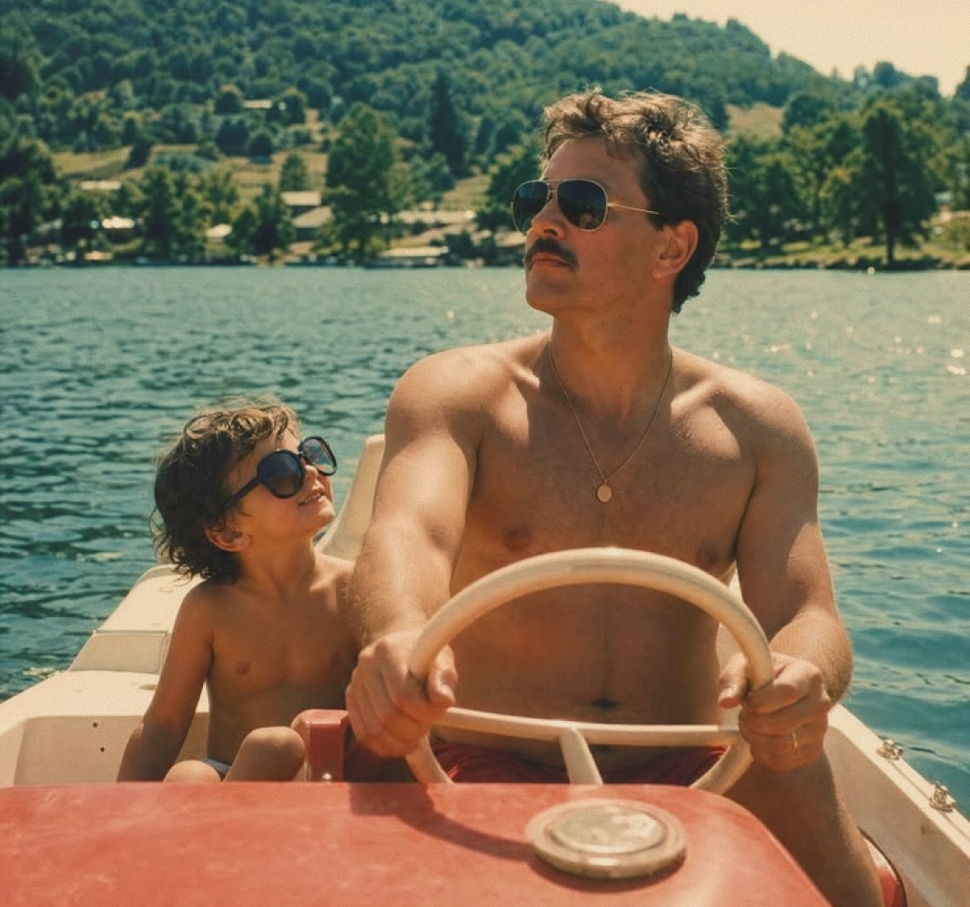 A father at the wheel of a small boat on a lake, his young son sitting beside him in sunglasses.